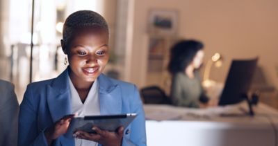 Woman working on tablet stands in foreground, while another woman works at desk behind her, Support Services | DXC Technology